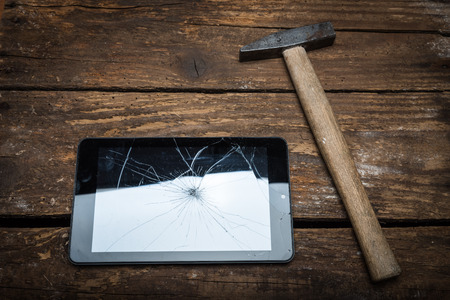 Hammer and tablet on the wooden table with broken glass.の写真素材