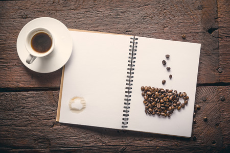 Notepad with cup of coffee made of beans and espresso on wooden desk. Stain on paperの写真素材