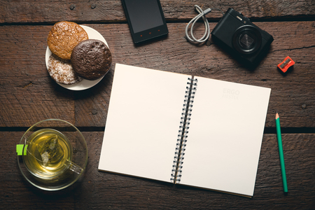 Blank opened notepad on the table, Cup of tea, honey-cakes, smatphone and camera.の写真素材