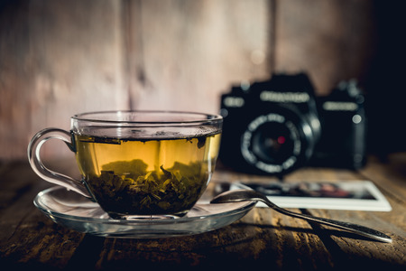 Glass cup of green tea, teaspoon and black analog camera on wooden table, picturesの写真素材