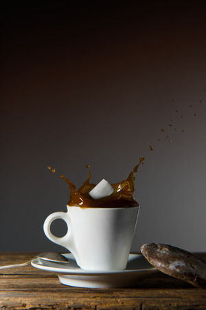 A white cup of esspresso with coffee splashed out, and sugar cube dropped into the liquid.の写真素材