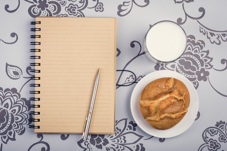 Roll, glass of milk or kefir and opened notepad with pen on the desktopの写真素材