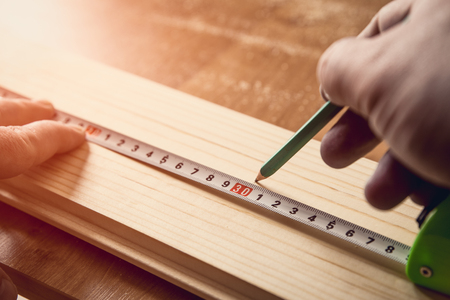 Carpenter measuring wooden board with setsquare and tape-measureの写真素材