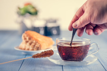 A glass cup of fresh hot black tea on the table. French cake in background.の写真素材