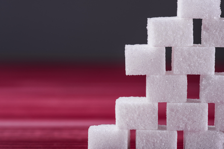 The wall built of sugar cubes on the red wooden tableの写真素材