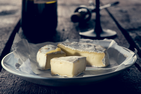Three sliced pieces of camembert cheese on the plate by the bottle of wine anf glassの写真素材