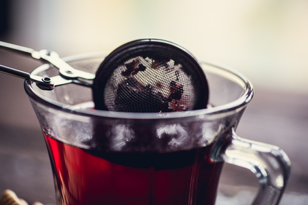 Glass of black or red tea or herbs in tea stainer on wooden tableの写真素材