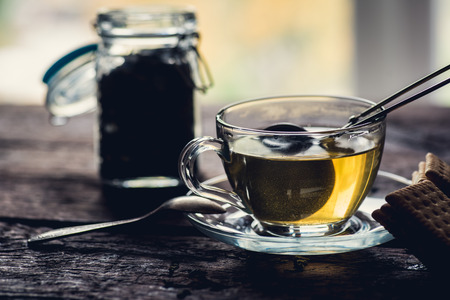 Glass of black or red tea or herbs in tea stainer on wooden tableの写真素材