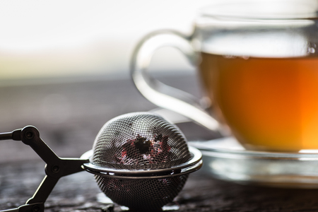 Glass of black or red tea or herbs in tea stainer on wooden tableの写真素材