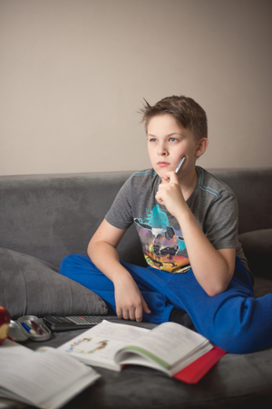 Young caucasian boy doing his homework sitting on the bed using calculator. Education concept.の写真素材