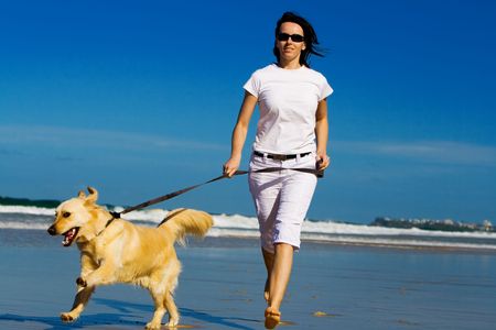 Young woman running on the beach with dogの写真素材