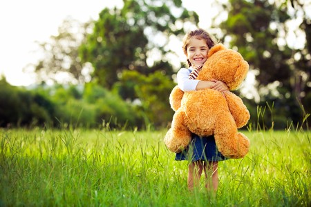 Little cute girl standing in the grass holding large teddy bearの写真素材