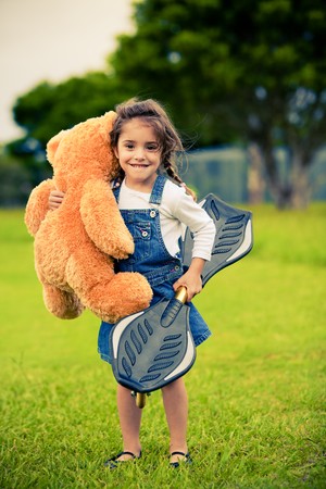 Little cute girl standing in the grass holding teddy bearの写真素材