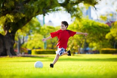 Young excited boy kicking ball in the grass outdoorsの写真素材