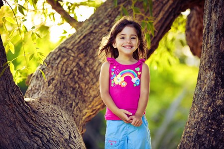 Smiling young girl standing on tree branches with green leavesの写真素材