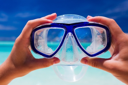 Hand holding snorkel googles against beach and skyの写真素材