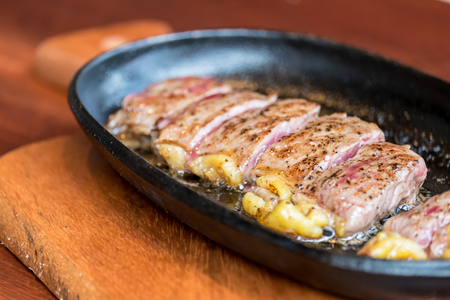 Beef steak in hot pan on wooden tableの写真素材