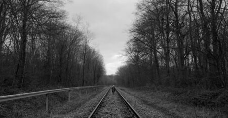 boy runs on a train tracks through the forest in the netherlandsの写真素材