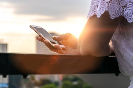 Woman typing write message on smartphone at sunset. Cropped image of young pretty girl with mobile phone.の写真素材