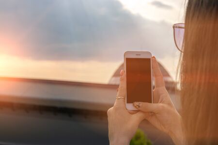 Girl makes a photo on the phone at sunset.の写真素材