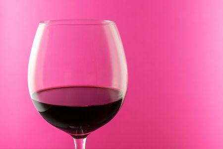 Studio shot of a glass of red wine isolated on pink background closeup. Clean and minimal. Red wine in a big glass. Wine concept.の写真素材