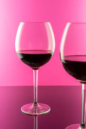 Studio shot of a glass of red wine isolated on pink background closeup. Clean and minimal. Red wine in a big glass. Wine concept.の写真素材