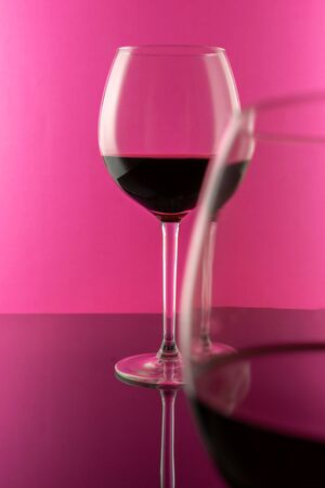 Studio shot of a glass of red wine isolated on pink background closeup. Clean and minimal. Red wine in a big glass. Wine concept.の写真素材