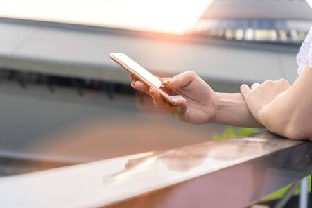 Woman typing write message on smartphone at sunset. Cropped image of young pretty girl with mobile phone.の写真素材