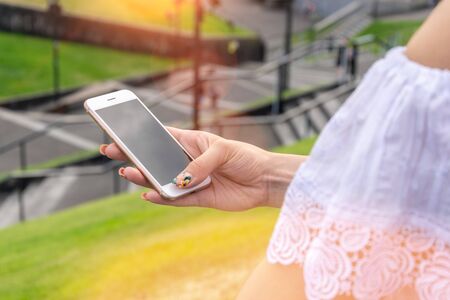 Woman typing write message on smartphone at sunset. Cropped image of young pretty girl with mobile phone.の写真素材