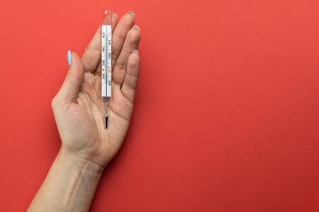 Pandemic background. Womans hands use thermometer to check temperature. Medical equipment on red background. Concept COVID quarantine. Coronavirus Preventive Measures.の写真素材