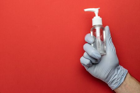 Gel hands on medical red background. Washing hands with antibacterial sanitizer gel in lab gloves. Clear sanitizer in pump bottle. Corona Virus pandemic protection by washing hands frequentlyの写真素材