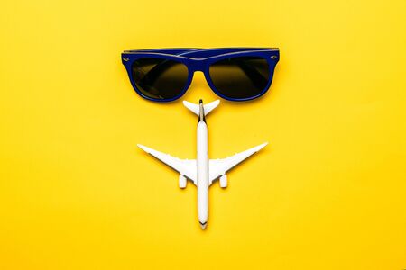 Travel background. White toy airplane and blue sunglasses on bright yellow backdrop. Flight vacation or fly in sky air plane vacation concept.の写真素材