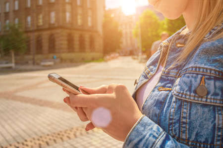 Lifestyle self. Happy young girl with phone smile, typing texting and taking selfie in summer sunshine urban city. Modern technology toothy laughter rest relax chill lifestyle conceptの写真素材