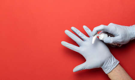 Using hand sanitizer alcohol gel on red background in Medical lab gloves. Clear sanitizer in pump bottle, for killing germs, bacteria. Corona Virus pandemic protection by washing hands frequentlyの写真素材