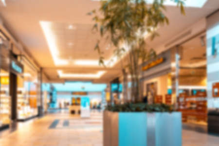 Shopping mall interior blurred background. People shopping in modern commercial mall center. Interior of retail centre store in soft focus. Image for background use.の写真素材