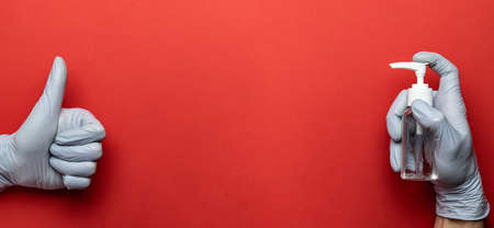 Medical gloves, antibacterial sanitizer gel - Virus protection equipment on red background. Clear sanitizer in pump bottle. Corona Virus pandemic protection by washing hands frequentlyの写真素材