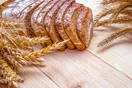 Whole wheat bread. Fresh loaf of rustic traditional bread with wheat grain ear or spike plant on wooden texture background. Rye bakery with crusty loaves and crumbs. Homemade bakingの写真素材