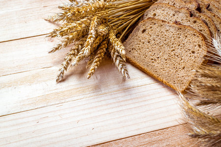 Whole wheat bread. Fresh loaf of rustic traditional bread with wheat grain ear or spike plant on wooden texture background. Rye bakery with crusty loaves and crumbs. Homemade bakingの写真素材