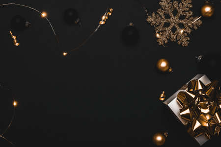 Christmas decoration isolated. White gift with golden bow, gold balls and sparkling lights garland in xmas decoration on dark background for greeting card. Decoration and copy space for your textの写真素材