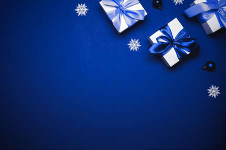 Winter background blue. White gift with cyan bow, blue balls and winter tree in xmas decoration on azure background for greeting card. Winter festive composition with copy spaceの写真素材