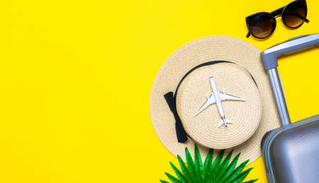 Summer pattern background. Suitcase, sunglasses with palm leaves and straw hat, white plane in travel composition on yellow background. Top view, flat lay. Copy spaceの写真素材
