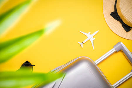Summer sale. Travel accessories with suitcase, white plane, palm leaves in minimal trip vacation concept on yellow background. Road frame set. Flat lay, top viewの写真素材