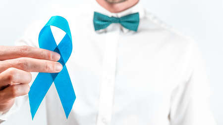 Blue prostate ribbon. Awareness cancer of men health. Hipster men in bright shirt, cyan bowtie with blue ribbon in hands on white background. November and International Mens Dayの写真素材