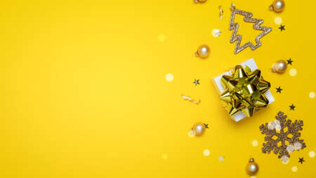 Winter banner. White gifts with golden bow, yellow balls and sparkling lights in xmas decoration on yellow background for greeting card. Flat lay, top view, copy space.の写真素材