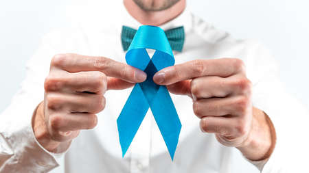Cancer people. Hipster men in bright shirt, cyan bowtie with blue ribbon in hands on white background. Awareness prostate cancer of men health. Man Healthcare and World cancer day conceptの写真素材