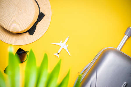 Summer background table. Suitcase, sunglasses with palm leaves and straw hat, white plane in travel composition on yellow background. Copy space, summer vacation and business travel conceptの写真素材