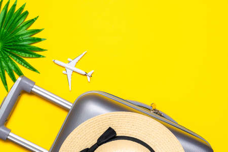 Summer pattern background. Suitcase, sunglasses with palm leaves and straw hat, white plane in travel composition on yellow background. Top view, flat lay. Copy spaceの写真素材
