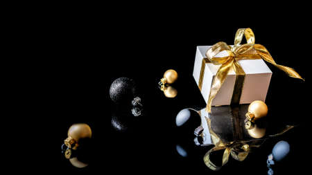 Happy new year. White gift with golden bow, gold balls and new year tree in Christmas decoration on dark background for greeting card. Winter festive composition with copy spaceの写真素材