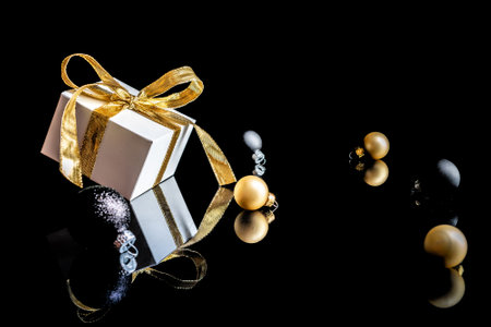 Xmas background gold. White gift box with golden ribbon, New Year balls and winter tree in Christmas composition on black background for greeting card. Copy space. Winter holidays, New Yearの写真素材