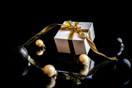 Gift boxes background. White gift box with golden ribbon, New Year balls and winter tree in...